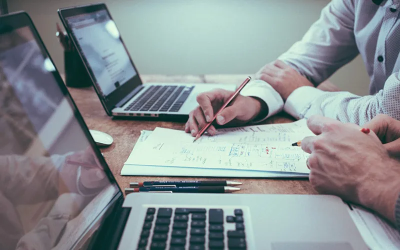 Zwei Personen arbeiten an Laptops und skizzieren eine Konstruktion auf Papier